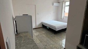 A small, clean room with a bed, a desk, and an air conditioning unit.