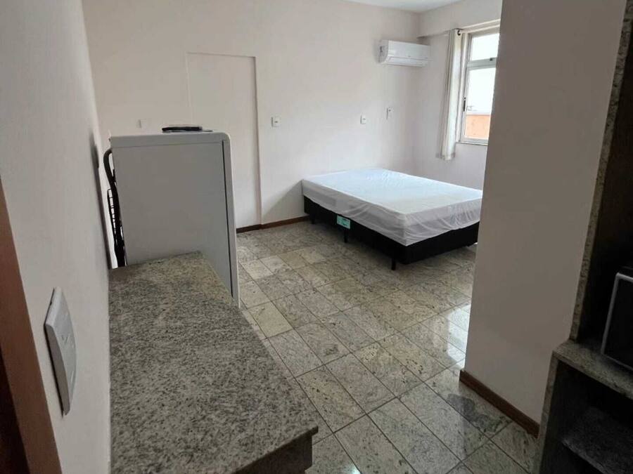 A small, clean room with a bed, a desk, and an air conditioning unit.