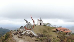 A hilltop with a church, a red-roofed building, and a large metal sculpture.