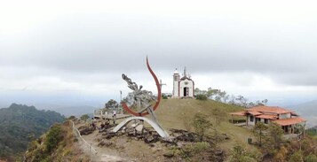 Uma colina com uma igreja, um edifício de telhado vermelho e uma grande escultura de metal.