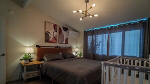 Een slaapkamer met een bed, nachtkastjes, een babybedje, een plafondlamp en kunst aan de muur.