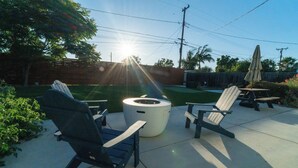 Een terras buiten met twee Adirondack-stoelen, een ronde tafel en een witte terrasverwarmer.