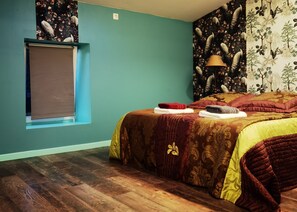 Une chambre avec des murs de couleur turquoise, un plancher en bois, un lit recouvert d’une couvre-lit à motifs et une fenêtre avec un rideau.