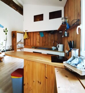 Een keuken met houten kastjes, een aanrecht en een spoelbak. Links staat een plant en rechts een raam.