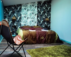 Ein Schlafzimmer mit einem Bett, einem Sessel, einem Teppich und einer Wand mit Pfauenmuster.