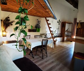 Ein Essbereich mit Holzbalkendecke, einem Tisch für vier Personen und einer Treppe, die zu einer oberen Ebene führt.