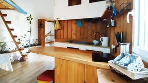 A kitchen with wooden cabinets, a sink, and a countertop. There is a plant on the left and a window on the right.