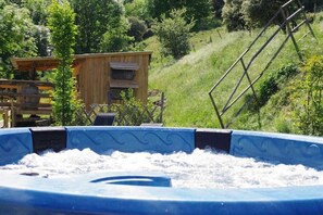 Un bain à remous entouré d’un chalet en bois et auquel on accède par une échelle en métal, le tout situé sur une colline verdoyante.