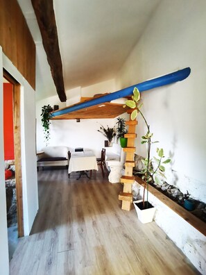 Een gezellige kamer met een houten wenteltrap, een zithoek met tafel en stoelen, en potplanten.