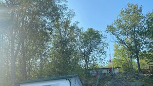 Une cabane dotée d’une terrasse en bois et d’un petit porche, entourée d’arbres et bordée d’une côte rocheuse.
