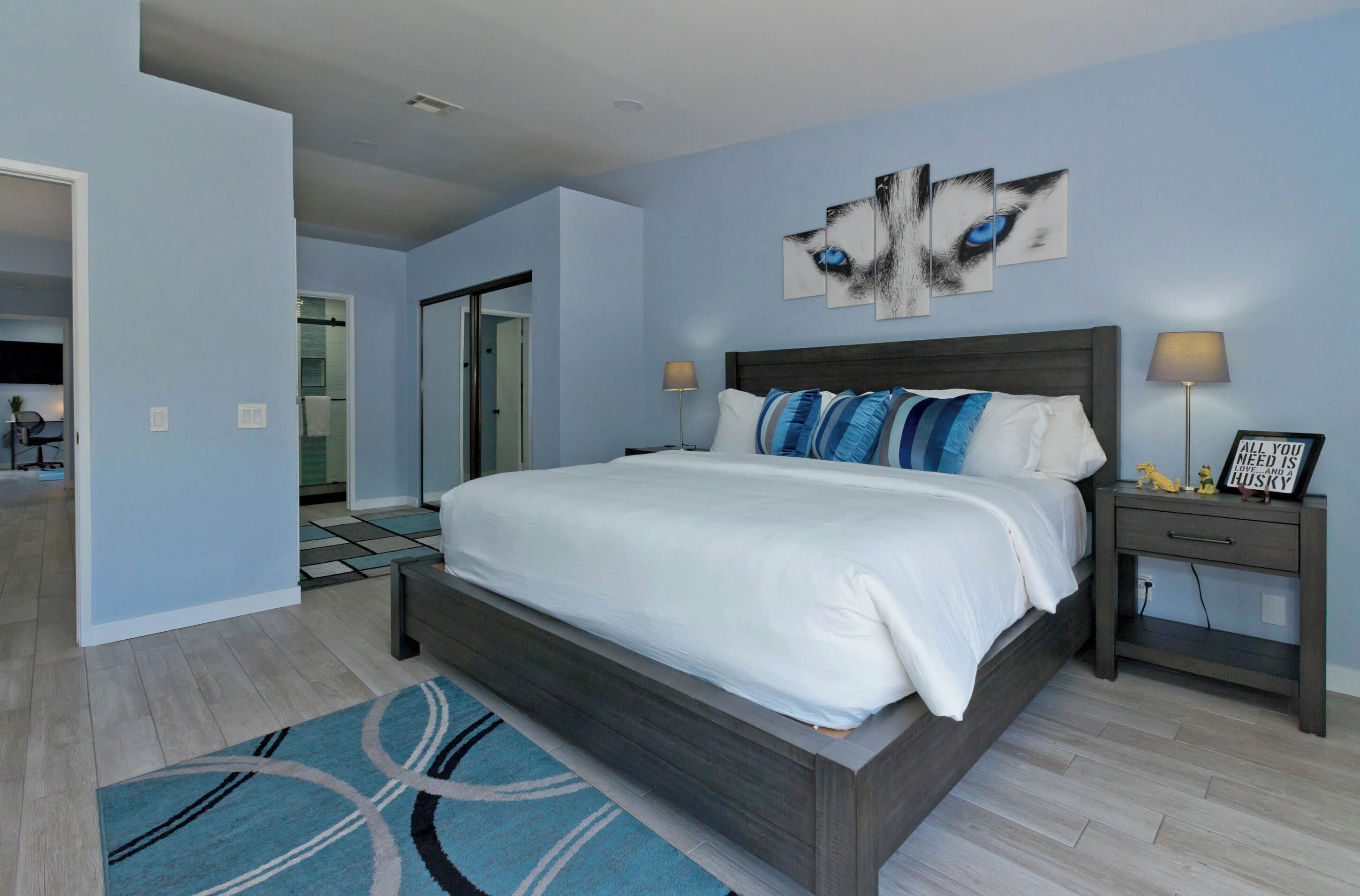 A modern bedroom with a large bed, a blue and white patterned rug, and a wall art piece.