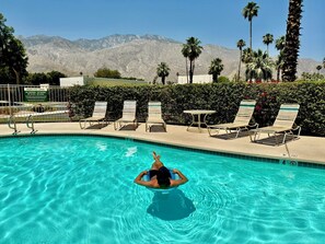 A swimming pool with clear blue water, surrounded by lounge chairs and a sign indicating no smoking, vaping, or dogs allowed.