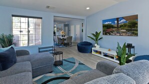 A modern living room with grey sofas, a coffee table, and a blue rug. There is a dining area in the background with a table and chairs. - Mojo Dojo Dog-Friendly 2BR/2BA in Mesquite Country Club by The Prescot Preserve (Palm Springs)