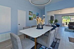 A modern dining area with a white table, grey upholstered chairs, and a decorative vase with pampas grass.