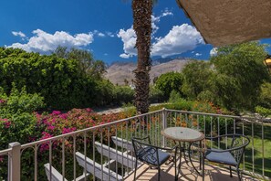 A balcony with a view of mountains, a palm tree, and a garden with colorful flowers.