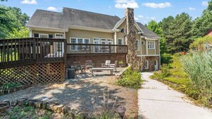 A two-story house with a stone chimney, a covered patio with outdoor furniture, and a fenced backyard. - 20 Acre Retreat Near Apex-Rentable Event Venue (New Hill)