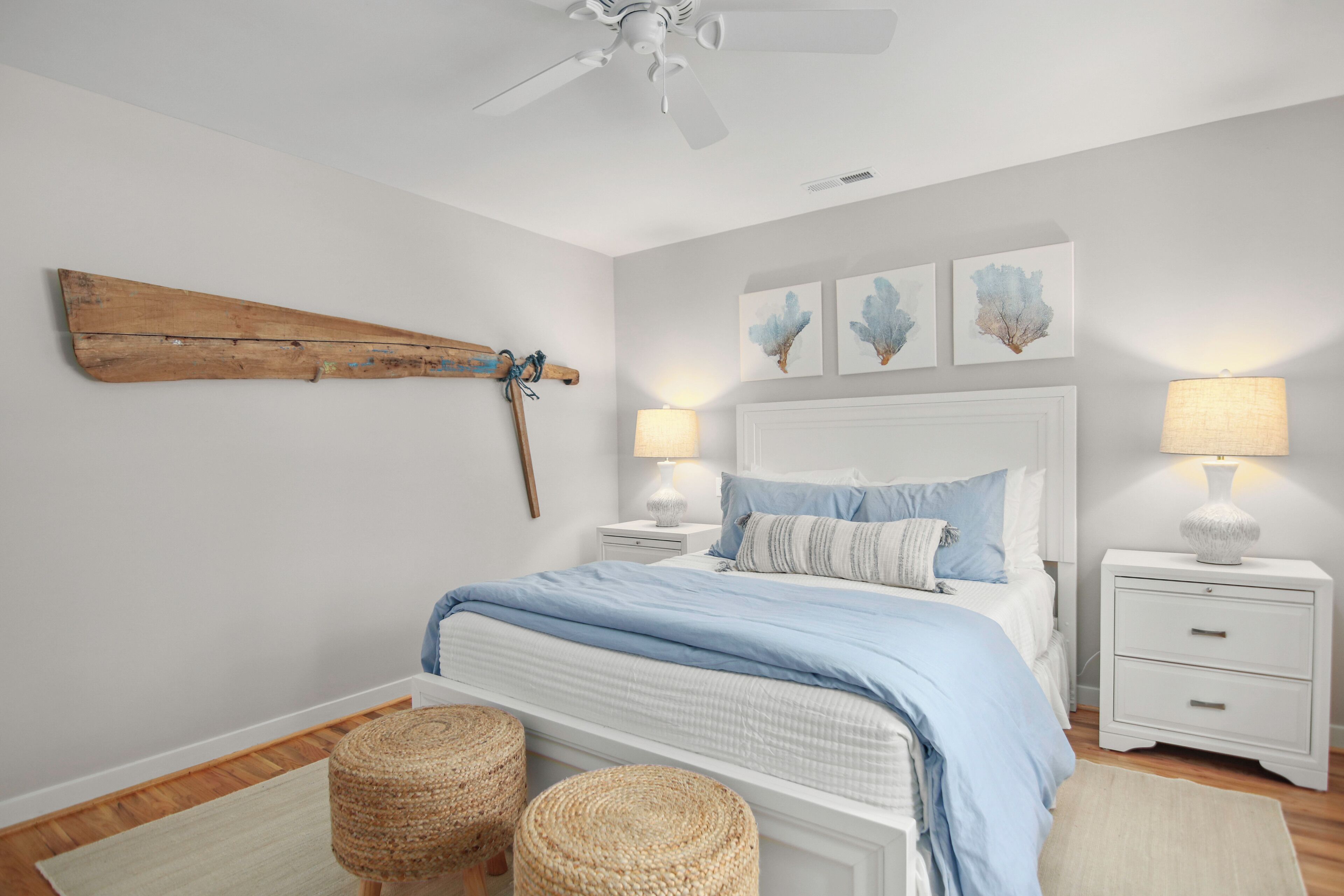 Une chambre à coucher comprenant un lit, deux tables de chevet, un ventilateur de plafond, un élément de décoration murale en bois et trois tableaux accrochés au mur.