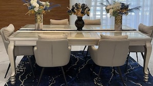 Un comedor moderno con una mesa de vidrio, cuatro sillas y dos jarrones con flores.