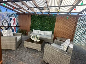 Ein Sitzbereich im Freien mit Korbmöbeln, einem Couchtisch mit Blumen und einem Wandbild mit dem Logo der Brooklyn Nets.