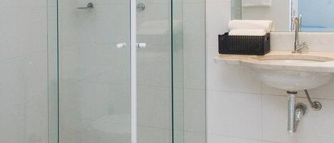 A modern bathroom with a glass-enclosed shower, a sink with a mirror, and a tiled floor.
