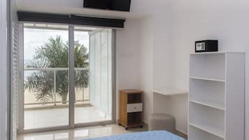 Un dormitorio con cama, puerta corrediza al balcón, un pequeño armario de madera y una estantería blanca.