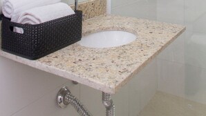 Une salle de bain moderne avec une douche à l’italienne en verre, un lavabo sur un plan de travail en granit et un panier noir contenant des serviettes.