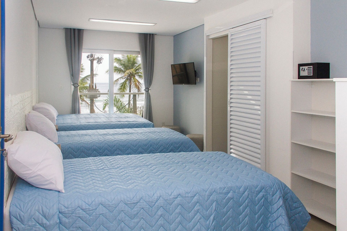 A hotel room with two beds, a TV on the wall, and a view of the ocean.