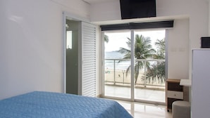 Une chambre avec un lit, un bureau et une vue sur la plage, accessible par une porte coulissante.