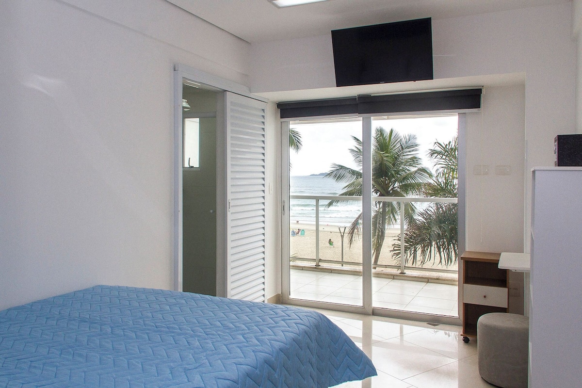 A bedroom with a bed, a desk, and a view of the beach through a sliding door.