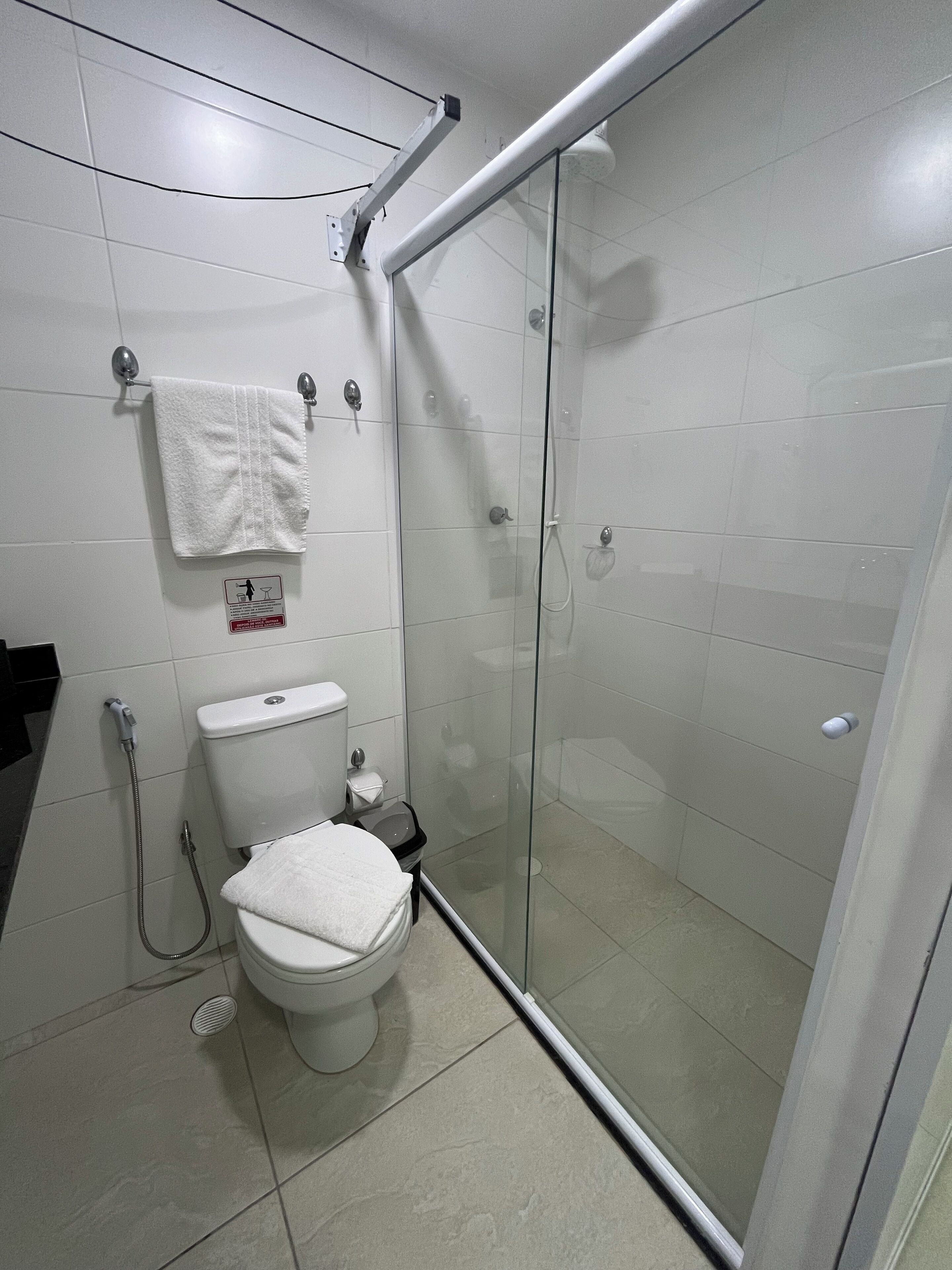 Un baño moderno con inodoro, cabina de ducha de vidrio y toalla en un perchero.
