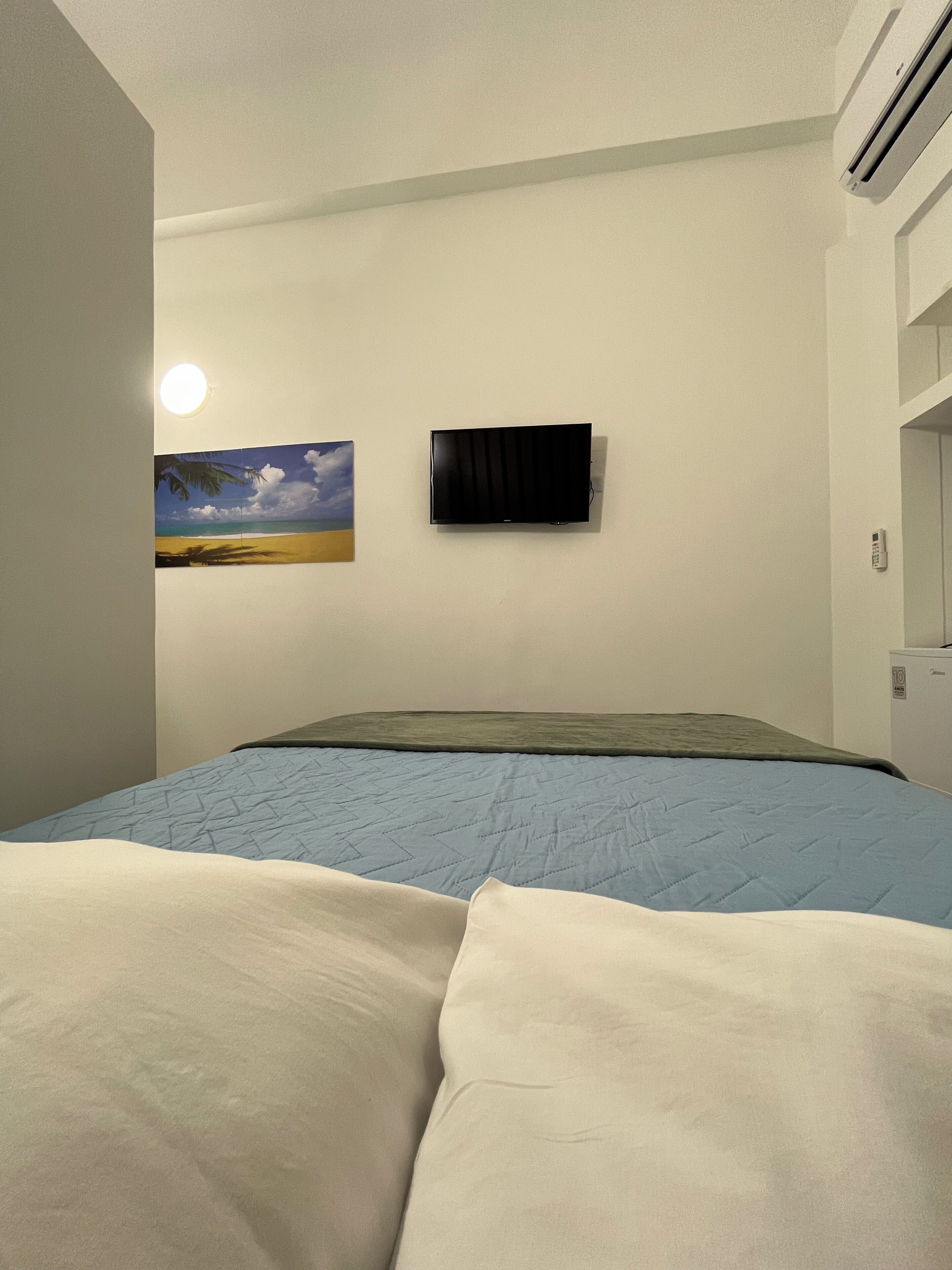 Un dormitorio con cama, un cuadro de una playa, televisión y aire acondicionado.