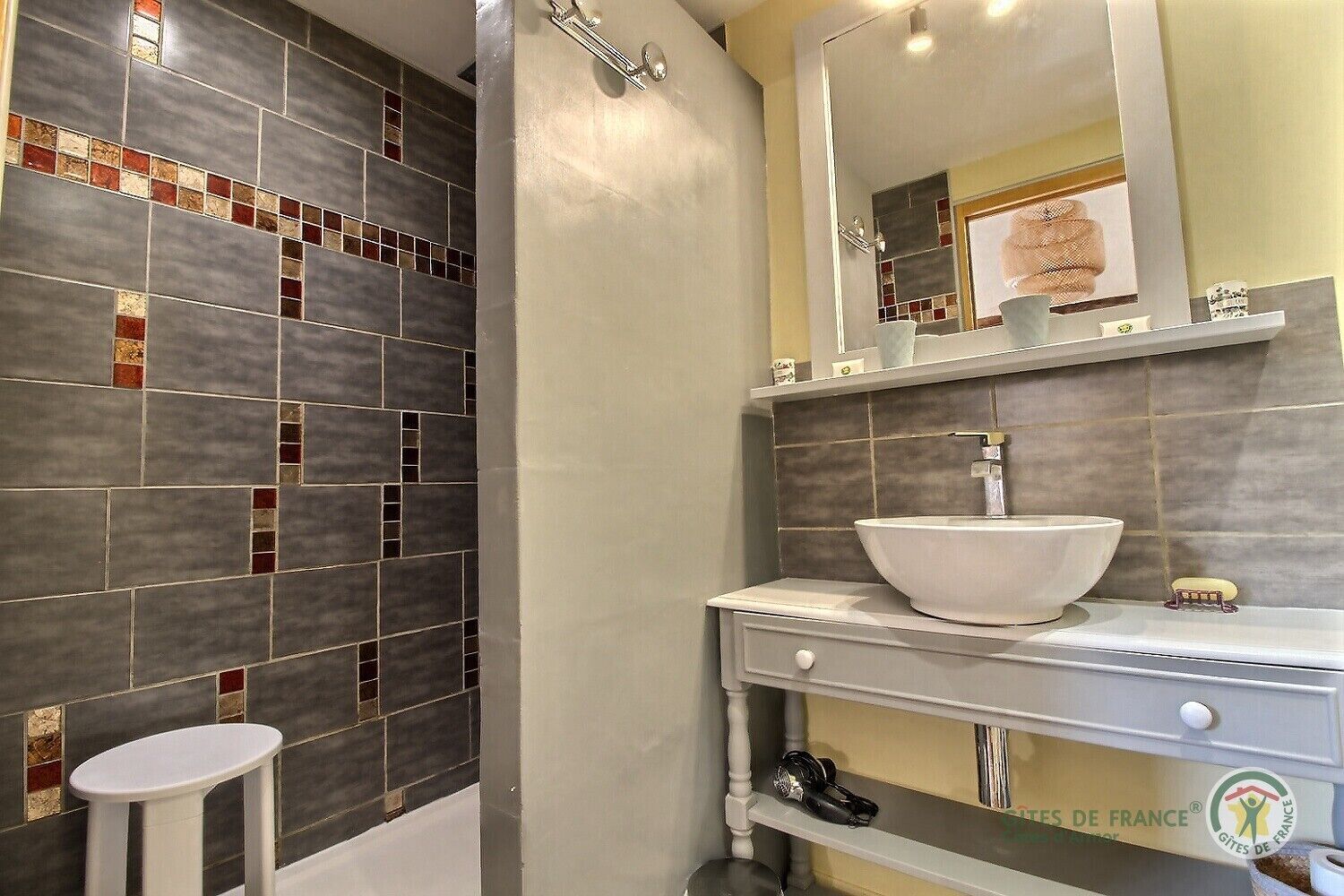 A bathroom with a large mirror, a white sink, and a tiled shower area.