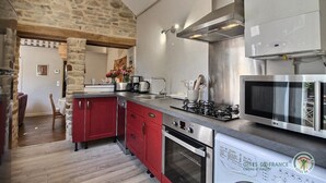 A modern kitchen with red cabinets, a stone wall, and stainless steel appliances including a microwave and stove. - Chez Isabelle - DINAN (DINAN)