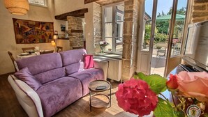 A cozy living room with a purple sofa, a small round table, and a view of the outdoors through large windows. - Chez Isabelle - DINAN (DINAN)
