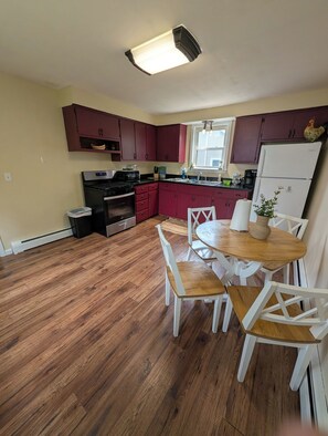 Una cocina con suelo de madera, una mesa de comedor con sillas, un refrigerador y una ventana.