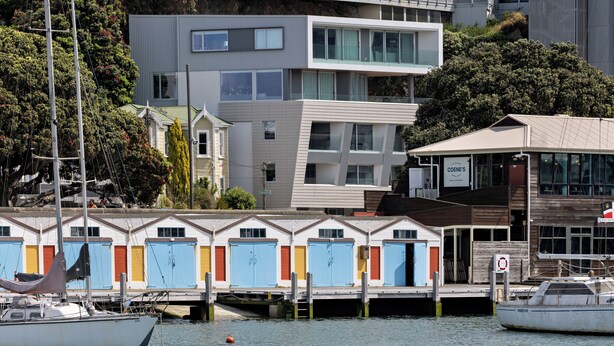 A waterfront property with a row of colorful cabins, a modern building, and a dock with boats. - U Suites on Oriental Parade (Wellington)