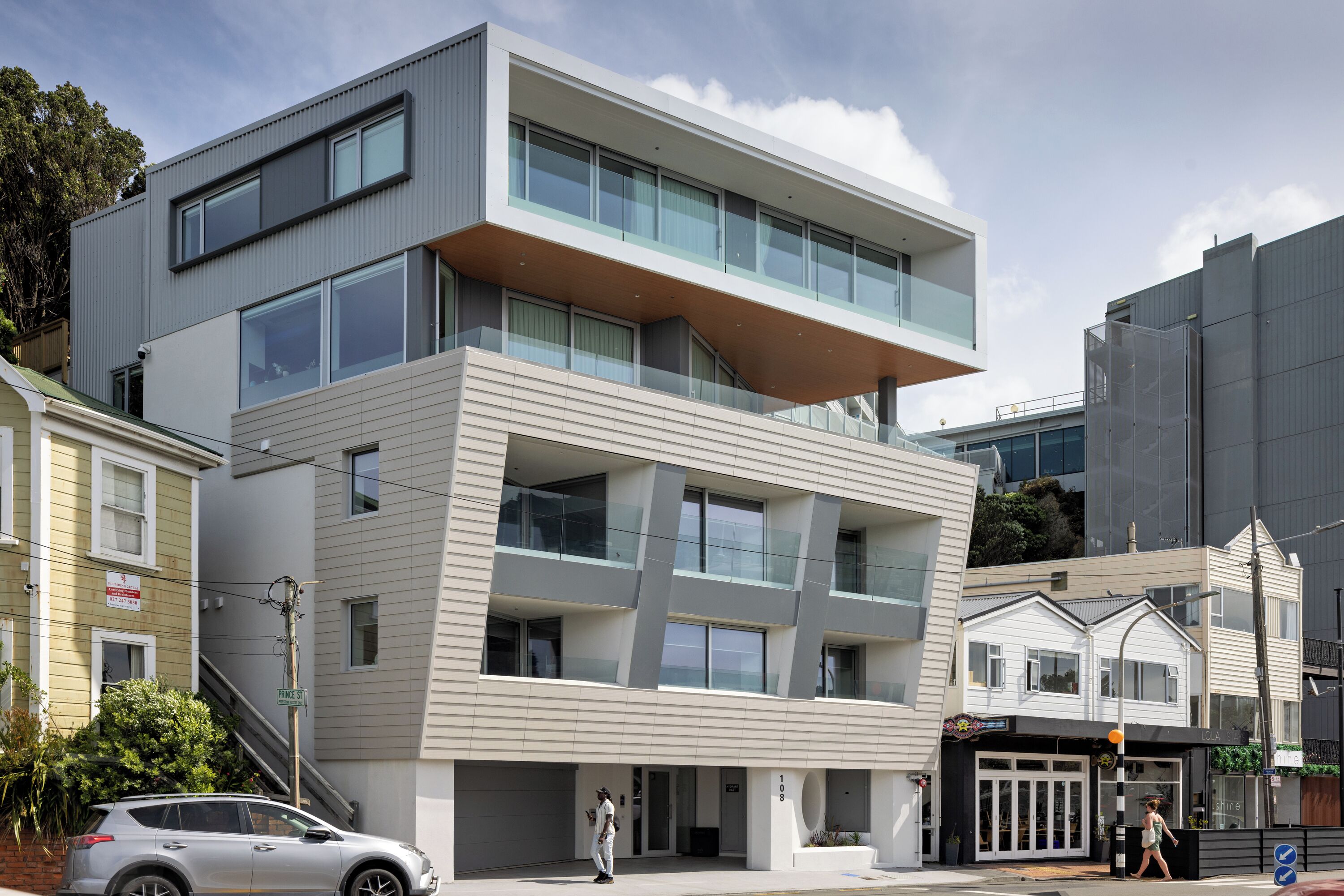 A modern multi-story building with a flat roof, large windows, and a balcony on the upper level.