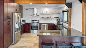 A modern kitchen with stainless steel appliances, dark wood cabinets, and a central island with bar stools.