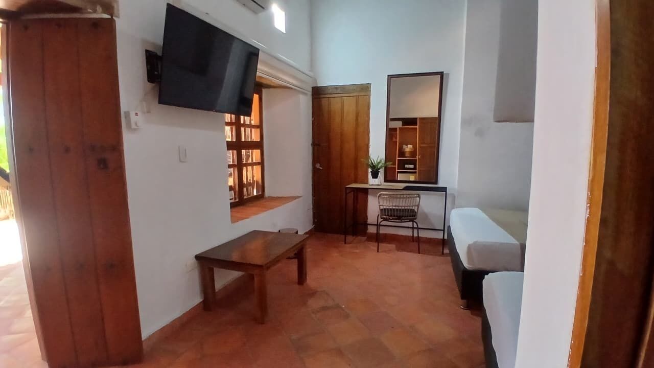 A living room with a TV mounted on the wall, a wooden cabinet, a bench, a desk with a chair, and a sofa.