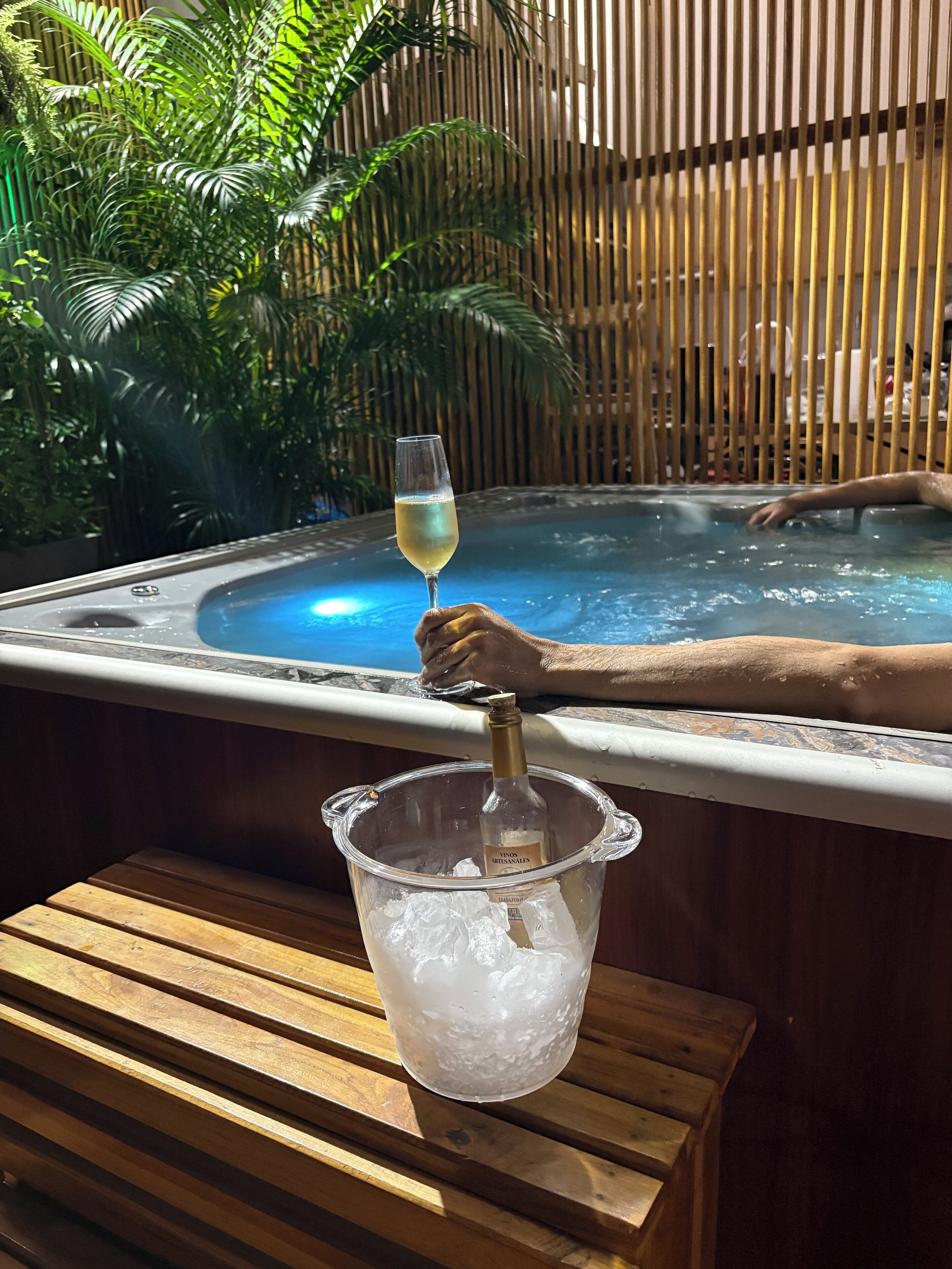 A hot tub with a wooden deck and a glass of white wine.