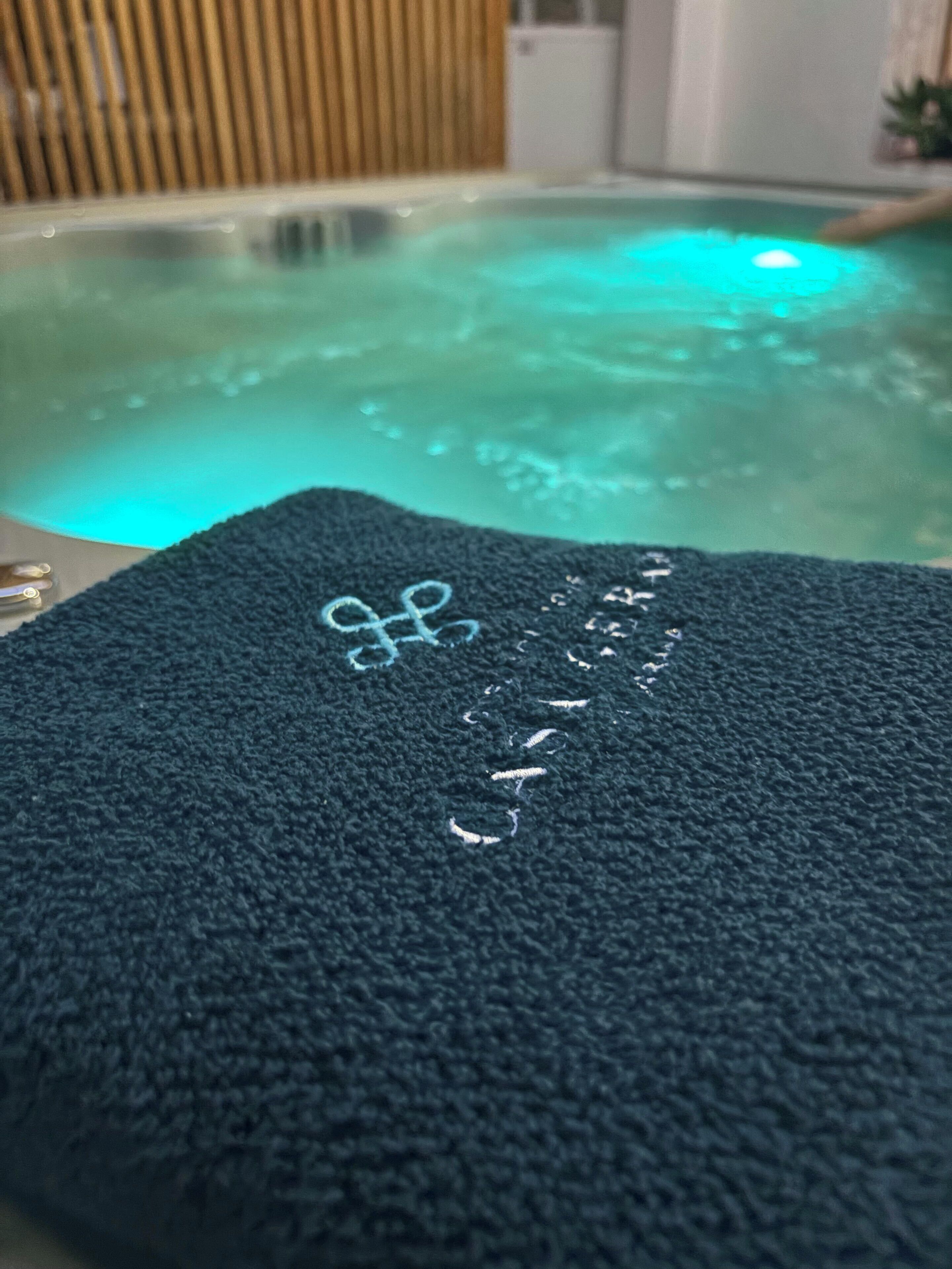 Une serviette bleu foncé ornée de motifs brodés, posée sur une surface près d’un bain à remous dont on peut voir les bulles.