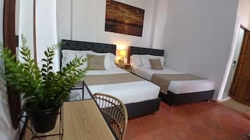 A hotel room with two beds, a wooden table, a potted plant, and a painting on the wall.