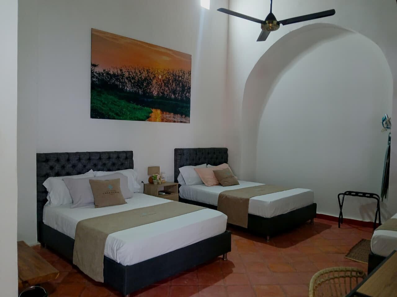 A hotel room with two beds, a ceiling fan, a painting, and a chair.