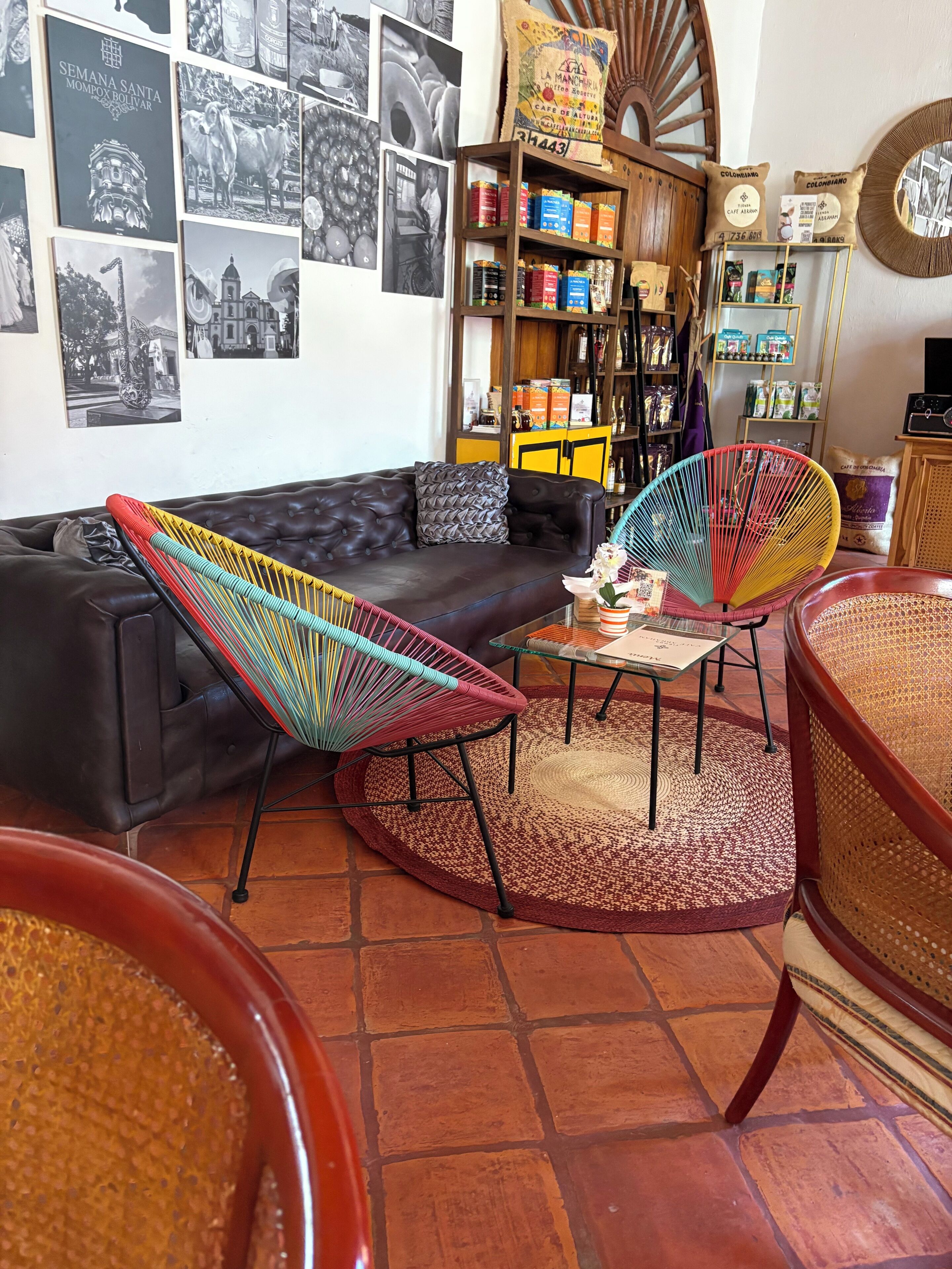 Uma sala de estar aconchegante com um sofá de couro preto, cadeiras coloridas de fibra natural e um canto para café.