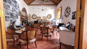 Une pièce spacieuse avec un haut plafond en bois, un sol carrelé et un coin repas comprenant des chaises et une table en osier.