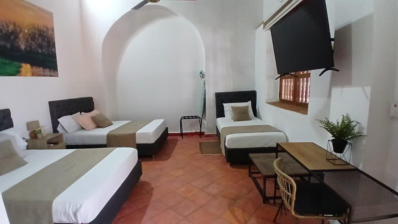 Een hotelkamer met twee eenpersoonsbedden, een slaapbank, een kleine tafel en een aan de muur bevestigde televisie.