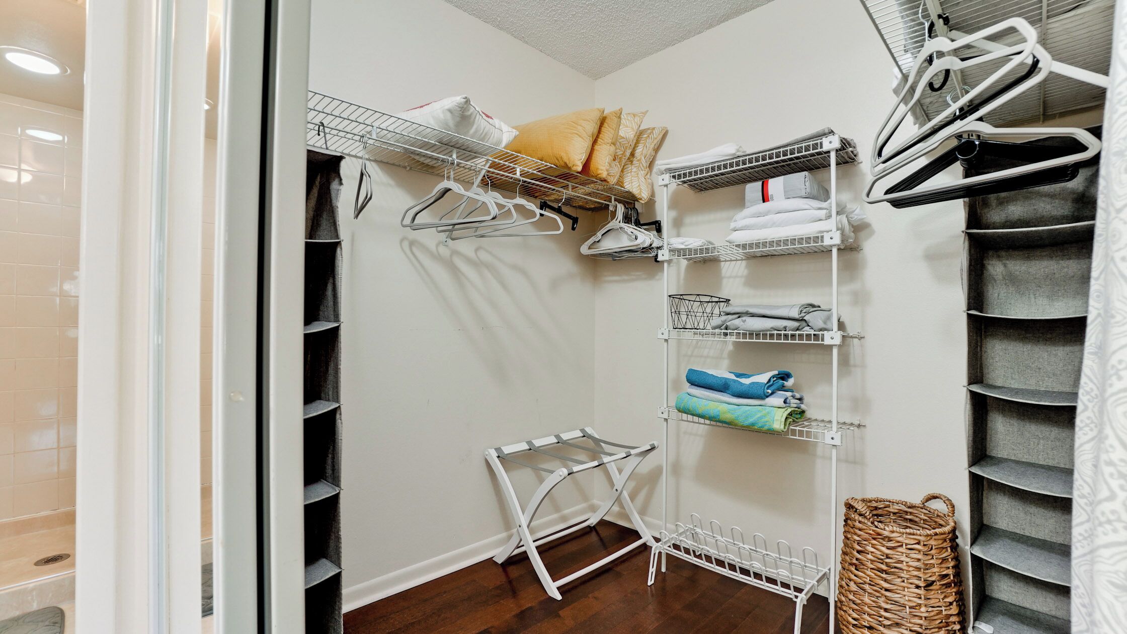 A walk-in closet with multiple shelves and hanging storage, featuring neatly folded clothes and a basket.