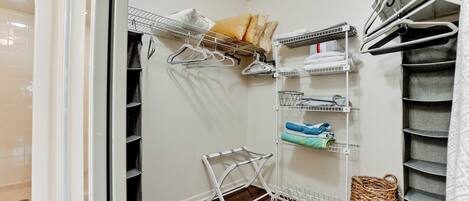 A walk-in closet with multiple shelves and hanging storage, featuring neatly folded clothes and a basket.