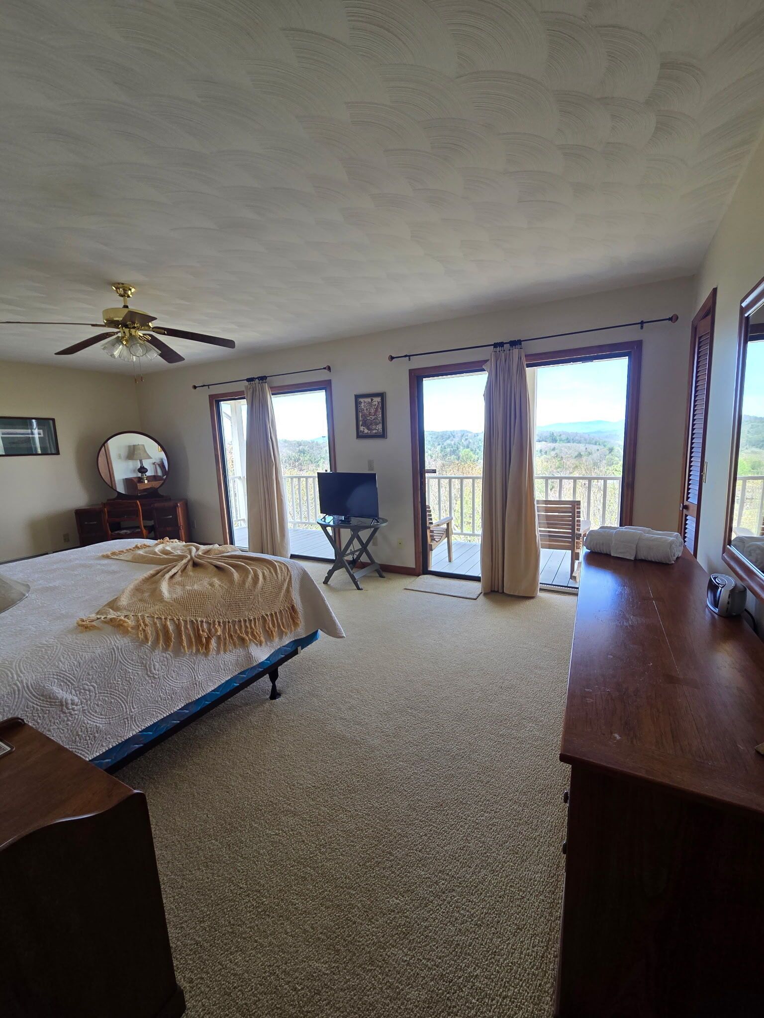 A bedroom with a bed, a desk, a chair, a television, and a balcony with curtains.