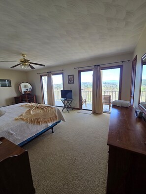 A bedroom with a bed, a desk, a chair, a television, and a balcony with curtains.